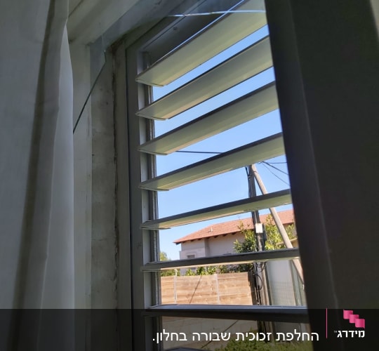 חלון עם זכוכית שבורה ותריסים פתוחים